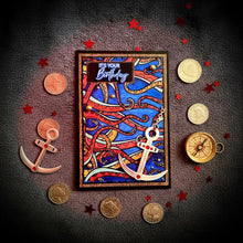Red Octopus Silver Anchor card flat lay on charcoal linen with red star confetti and compass